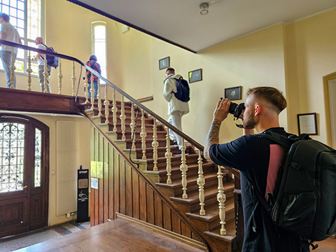 Mężczyzna fotografuje wnętrze budynku, skupiając się na ich architekturze i detalu, obok niego widać schody