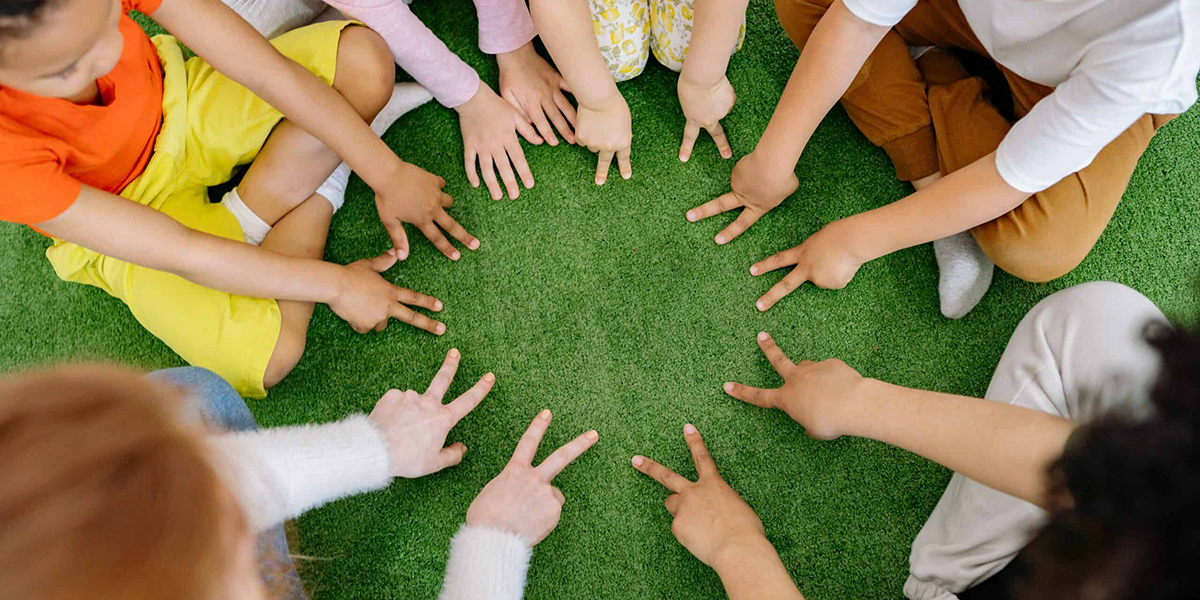 na zdjęciu widać wyciągnięte ręce dzieci siedzących w kółku, ich palce tworzą okrąg