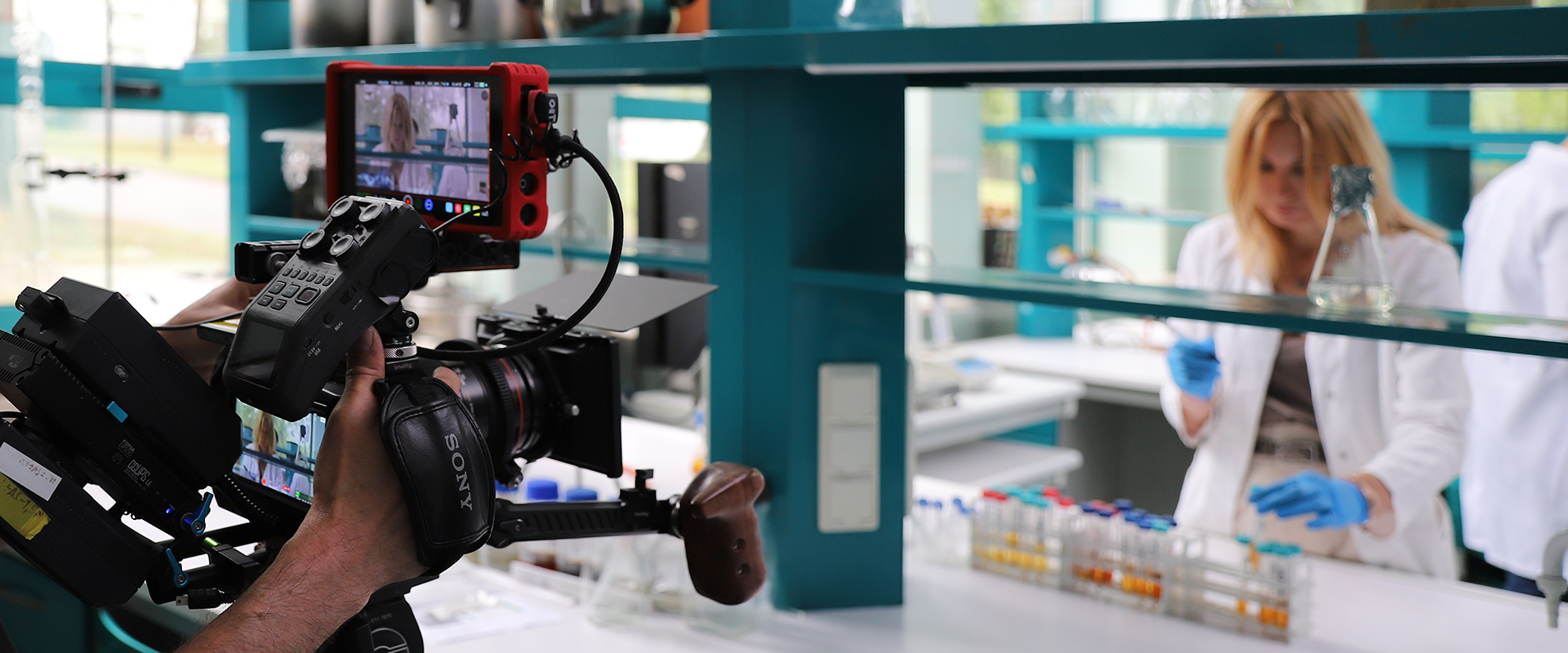 operator kamery filmuje prace w laboratorium, widać zbliżenie na jego ręce i kamerę