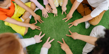 na zdjęciu widać wyciągnięte ręce dzieci siedzących w kółku, ich palce tworzą okrąg
