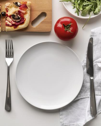 Na białym stole pusty talerz, obok nóż, widelec i serwetka