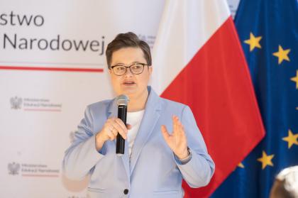 Kobieta w okularach wygłasza przemówienie na konferencji.