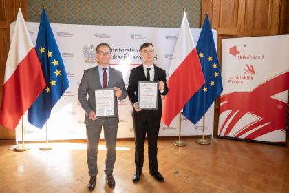 Mężczyźni w garniturach prezentują certyfikaty przed flagami.