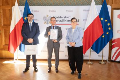 Grupa trzech ludzi z nagrodą, w tle flagi.