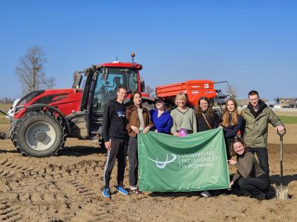 Grupa ludzi stoi przed traktorem, trzymając zieloną flagę