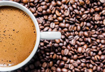 Filiżanka kawy, wokół niej rozsypane ziarna kawy